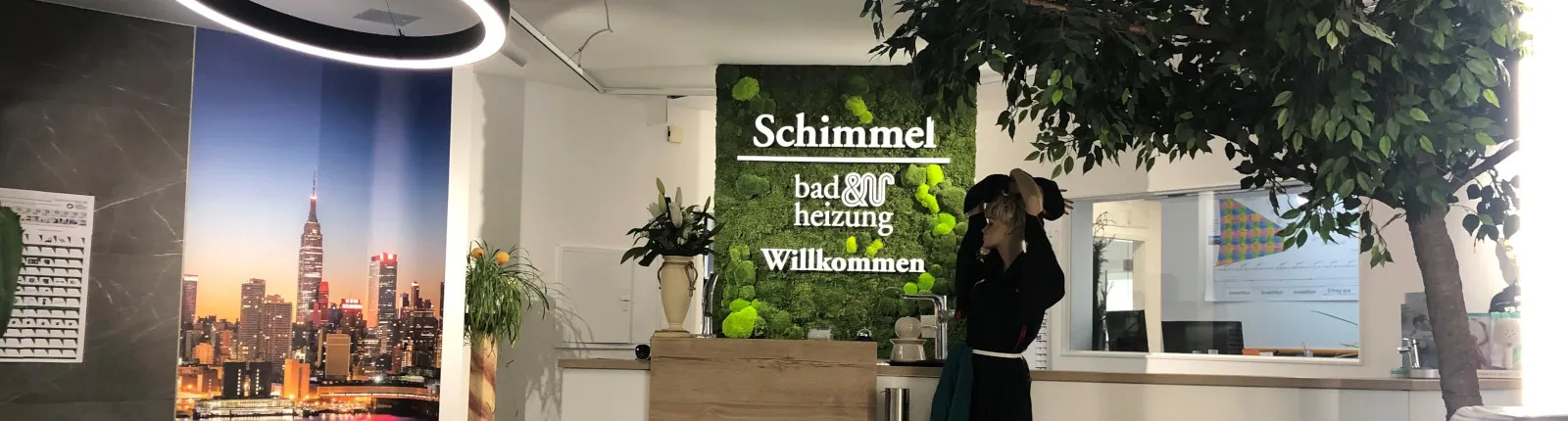 In einem freundlich gestalteten Empfangsbereich begrüßt eine grüne Mooswand mit dem Schriftzug „Schimmel – bad und heizung – Willkommen“ die Besucher. 