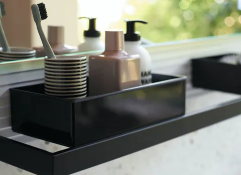 Nahaufnahme eines schwarzen Regals mit Zahnbürste, Zahnbürstenhalter und zwei Seifenspendern in Beige und Weiß.