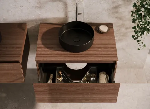 Der minimalistische Waschtisch der Kollektion Lin20 von burgbad zeigt ein rundes, schwarzes Aufsatzwaschbecken auf einer hölzernen Oberfläche.
