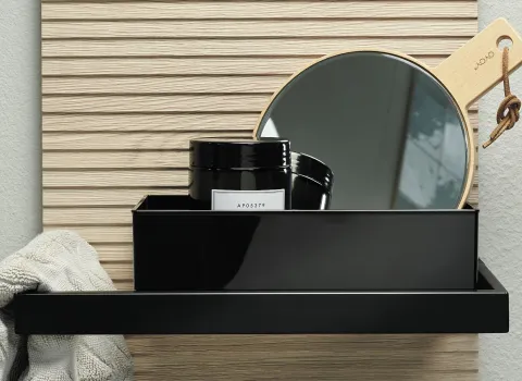 Ein schwarzes Aufbewahrungsfach an einer hellen Holzverkleidung, gefüllt mit einem Handspiegel und zwei schwarzen Kosmetikdosen.