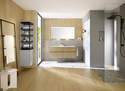 Eine schlichte Handtuchleiter aus schwarzem Metall steht in einem modernen Badezimmer neben einem Holzwaschtisch mit einem beleuchteten Spiegelschrank.