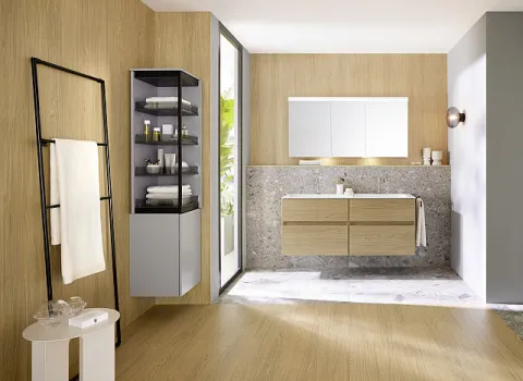 Eine schlichte Handtuchleiter aus schwarzem Metall steht in einem modernen Badezimmer neben einem Holzwaschtisch mit einem beleuchteten Spiegelschrank.