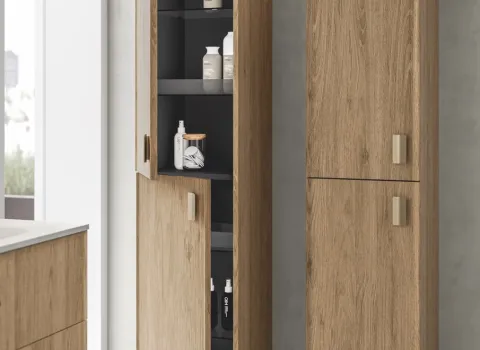 Hochschrank in warmer Holzoptik mit goldfarbenen Griffen, teilweise geöffnet mit sichtbaren Ablagefächern.