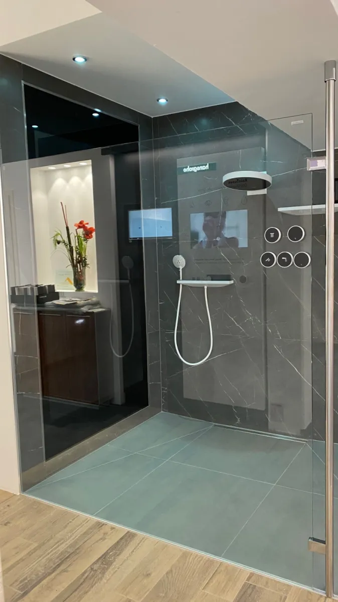 Eine moderne, bodenebene Dusche mit großformatigen grauen Fliesen und Glasabtrennung steht in einem hochwertig gestalteten Bad.