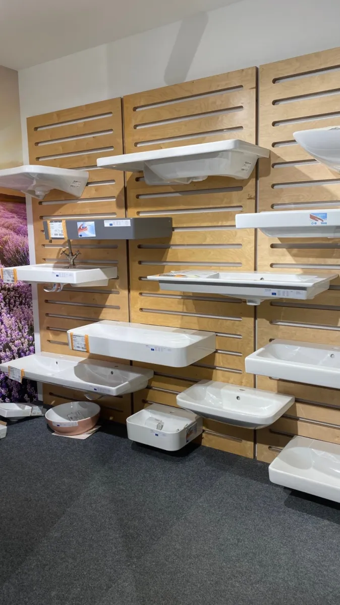 Mehrere Waschbeckenmodelle in verschiedenen Größen und Formen sind an einer Ausstellungswand mit Holzverkleidung montiert.