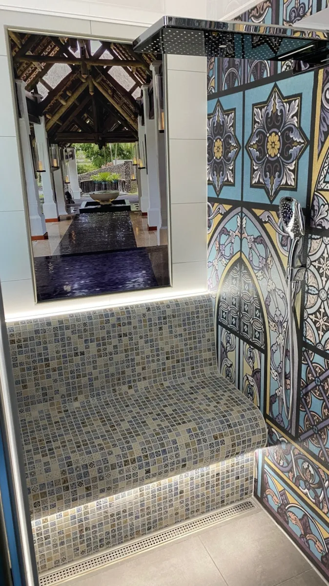 Ein luxuriöser Duschbereich zeigt eine geflieste Sitzbank mit LED-Unterleuchtung und eine Wandverkleidung in kunstvoller Kirchenfenster-Optik.
