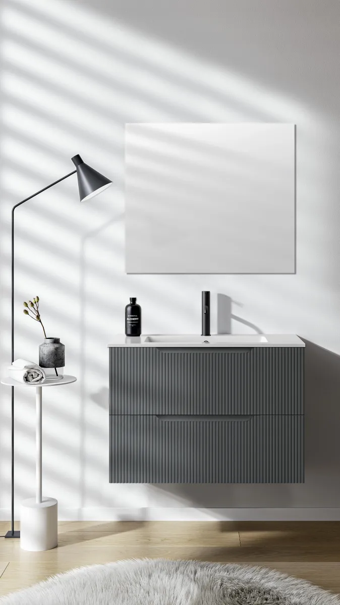 Modernes Badmöbel mit geriffelter Front in Grau unter quadratischem Spiegel und seitlicher Stehlampe.
