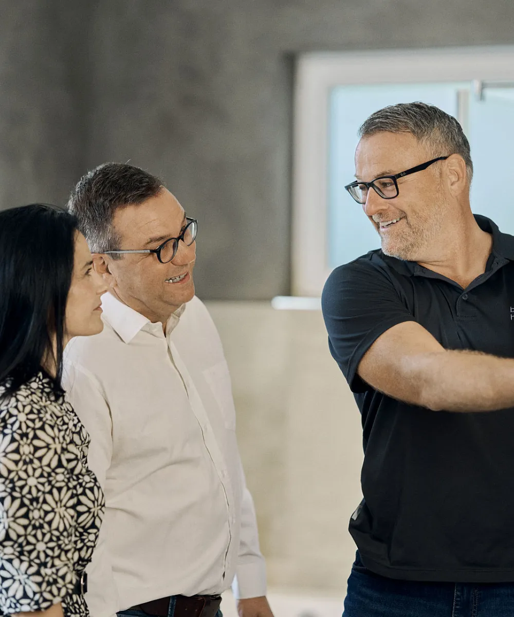 Ein Fachmann präsentiert einem interessierten Paar eine Dusche in einer Badausstellung. Alle drei lächeln, während sie die hochwertigen Produkte begutachten.