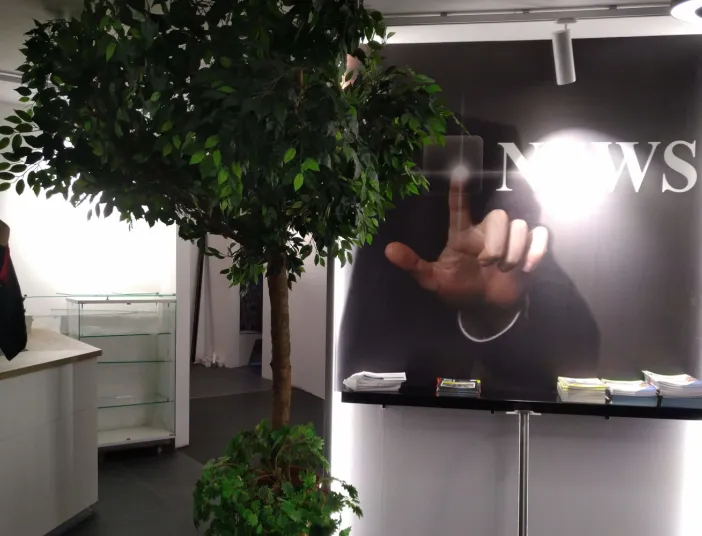 Ein beleuchtetes Wandmotiv mit der Aufschrift „NEWS“ zeigt eine Hand, die auf einen transparenten Bildschirm deutet.